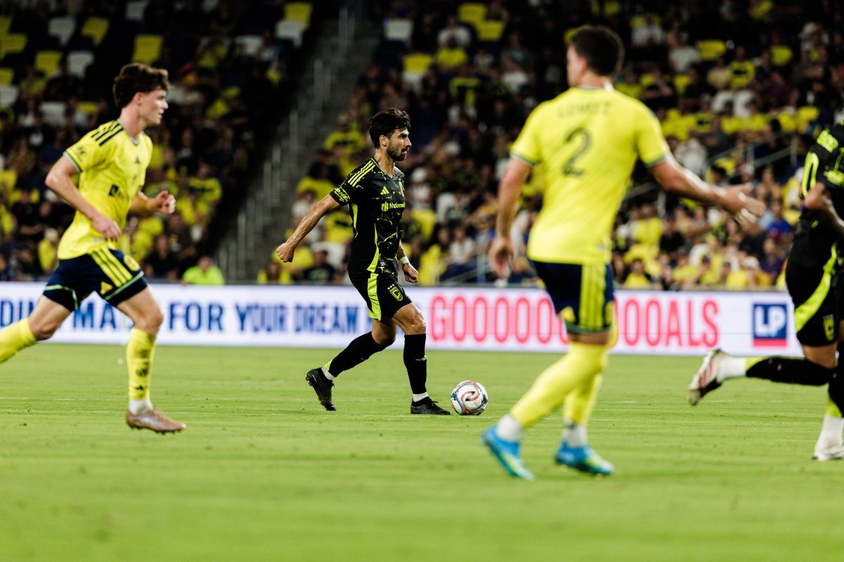 Player in black kit dribbles ball surrounded by yellow-kitted opponents