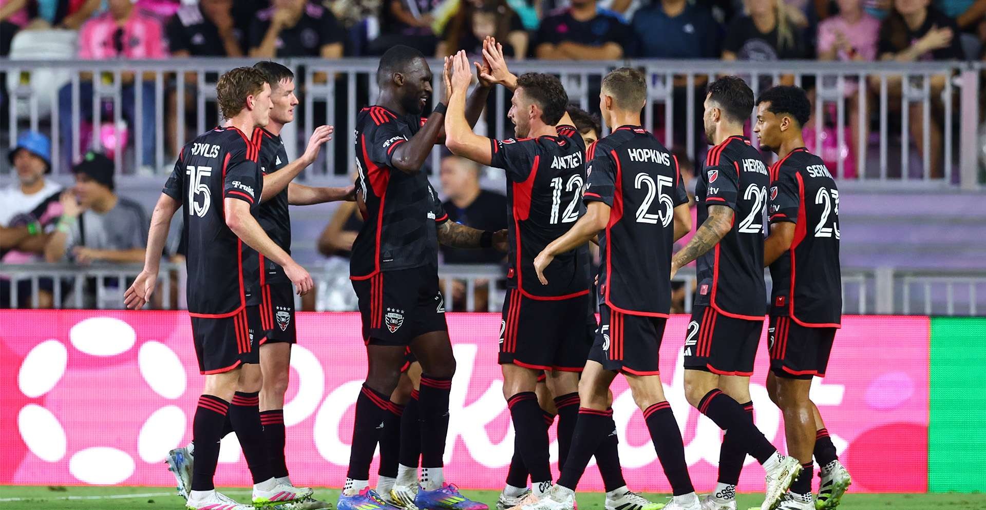 D.C. United players celebrate together on the pitch at night — Charlotte vs DC United